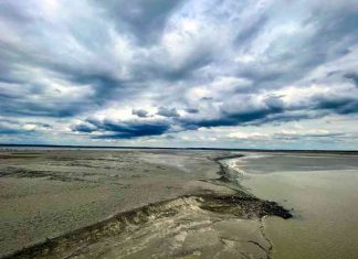 A serene beach with calm waters beneath a cloudy sky.