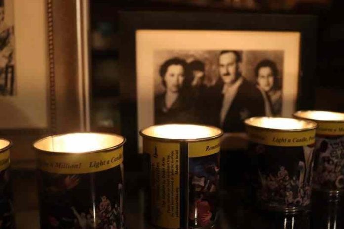 Four lit remembrance candles sit in front of a framed sepia-toned photo of a family.