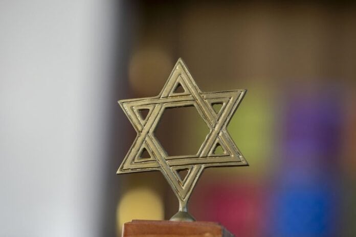 A brass Jewish star stands on a wooden base against a blurred background.