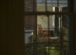 7:18 Gazing through a window, we look out on a porch with two rocking chairs, framed by greenery.