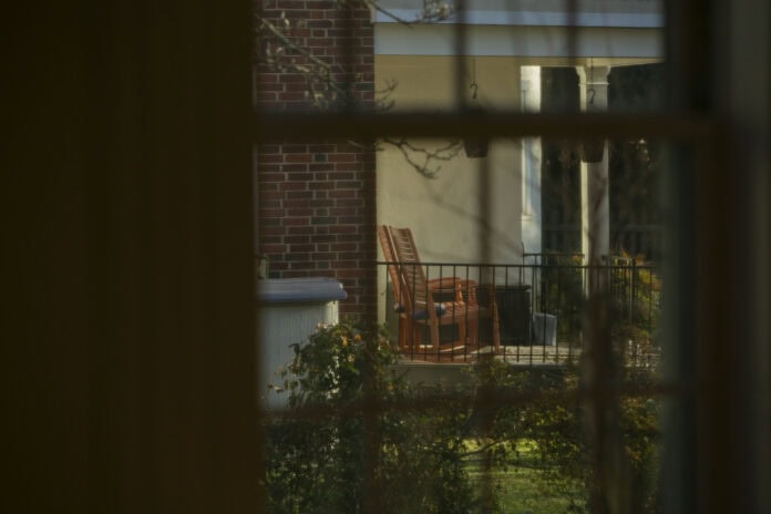 Gazing through a window, we look out on a porch with two rocking chairs, framed by greenery.
