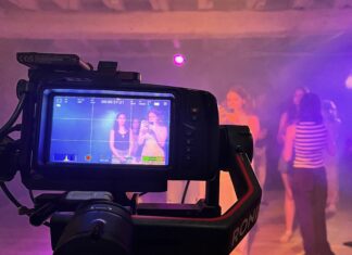 Directed By? A camera films a group of people in a dimly lit room with purple lighting; the camera display shows two women posing.