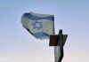 Over the Atlantic A tattered Israeli flag flies on a post against a pale blue sky.