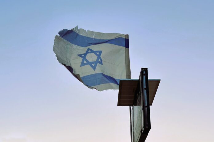 Tattered Hope A tattered Israeli flag flies on a post against a pale blue sky.