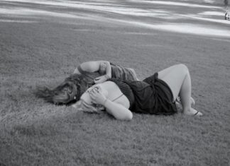 Black and white photo of two girls lying on the grass, laughing.