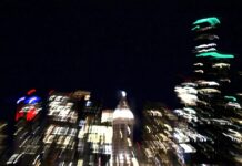 A blurry scene of a city at night. Buildings glow in the darkness.