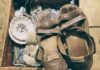 A pair of brown leather sandals, stained with wear, sit atop a wooden crate filled with antique objects.