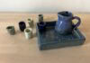Kiddush Set Naama Raun's Kiddush set includes a blue pitcher with five small individual cups. The pitcher and one of the individual cups sits on a ceramic tray decorated with floral print.