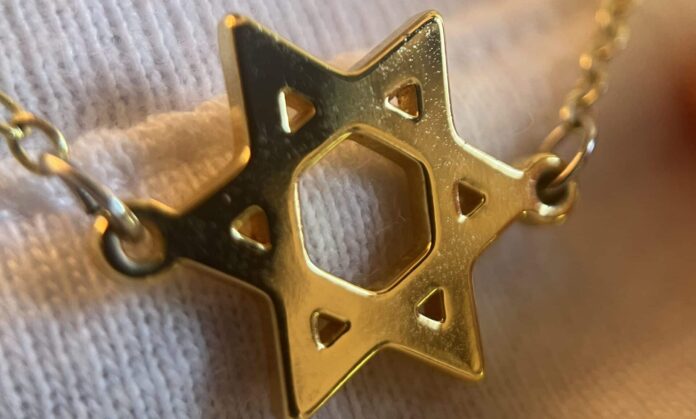 A gold Jewish star hangs on a necklace chain over a white shirt.