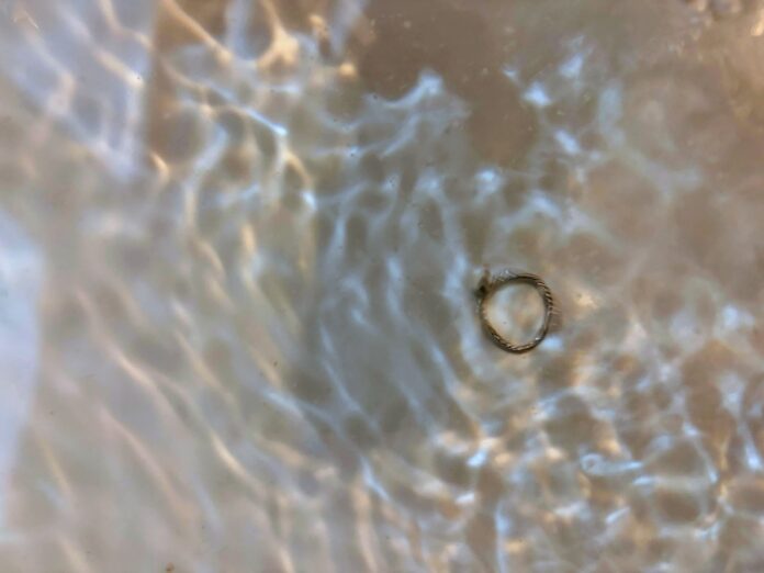 Close-up of a small silver ring in shallow water with sunlight creating wavy ripples across the water's surface