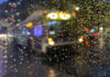 A city bus seen through a pane of glass covered in raindrops. The image is blurry.