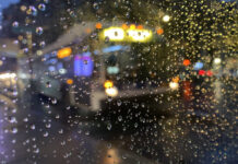A city bus seen through a pane of glass covered in raindrops. The image is blurry.