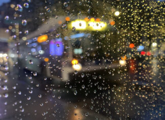 A city bus seen through a pane of glass covered in raindrops. The image is blurry.