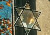 Standing A crystal Jewish star hangs in a lit window, refracting the natural light.