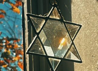 A crystal Jewish star hangs in a lit window, refracting the natural light.