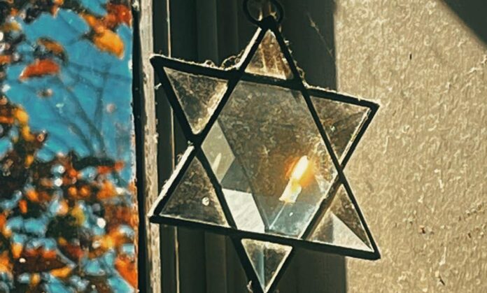 A crystal Jewish star hangs in a lit window, refracting the natural light.