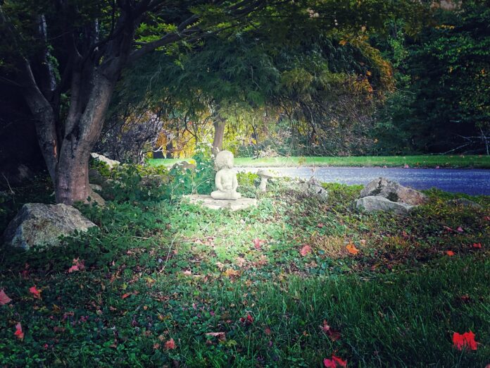 The Sturdy Child A soft halo of light surrounds a small statue of a child in a lush garden.