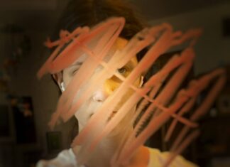 Girl looking into a mirror. Red marks drawn on the glass cover her face.